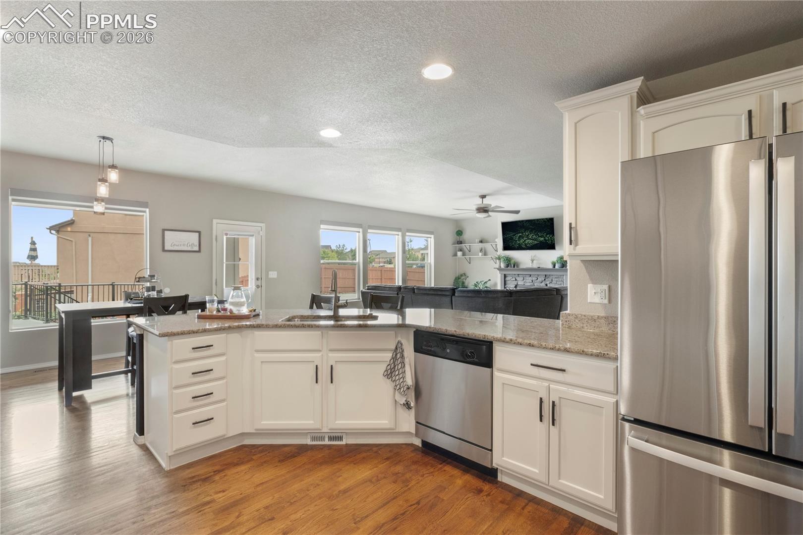 Kitchen with stainless steel appliances, a peninsula, white cabinetry, light wood-style flooring, and light stone counters