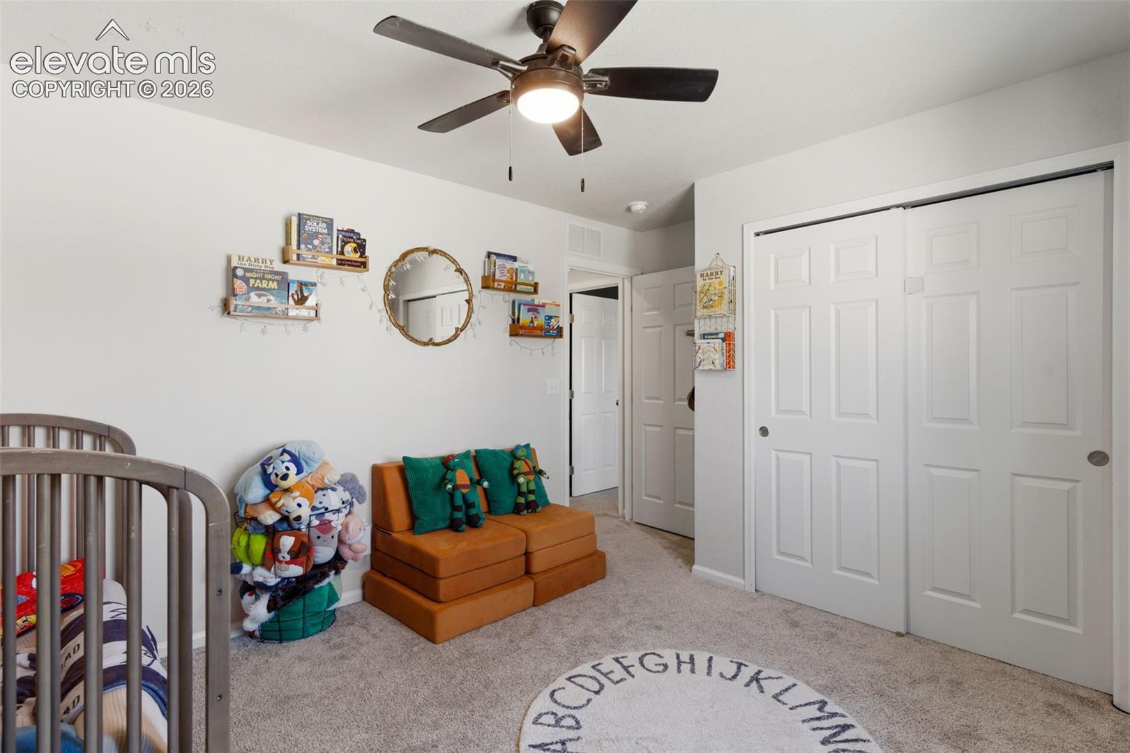 Spacious room featuring light gray carpeting, neutral wall paint, a ceiling fan with integrated lighting, and white bi-fold closet doors