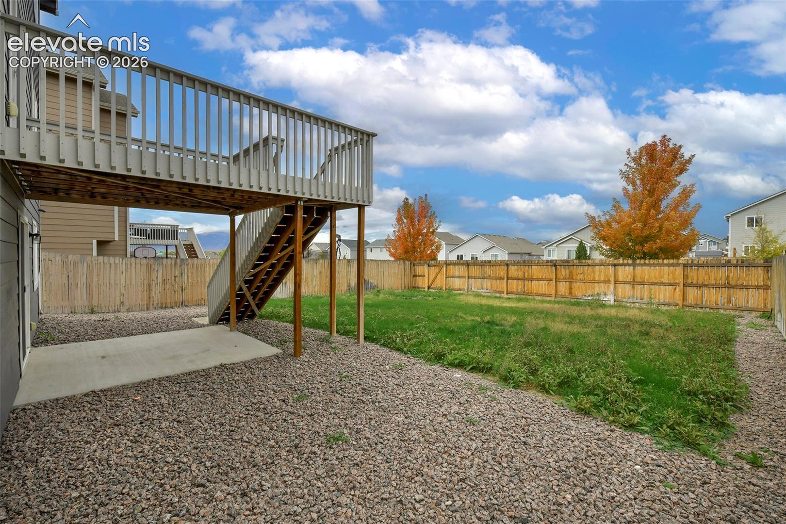 Rear exterior featuring an elevated wood deck with stairs, a concrete patio, and a fully enclosed wood privacy fence