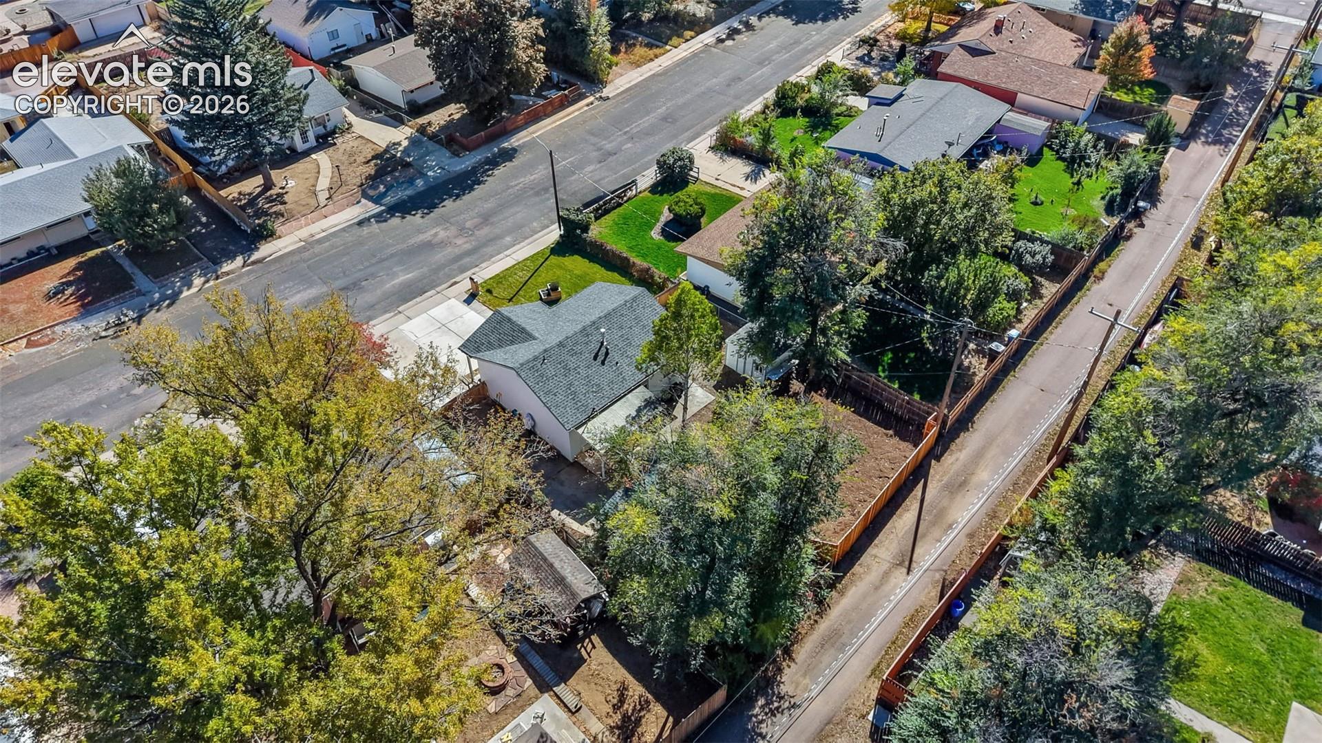 Aerial perspective of a corner lot property featuring a single-story structure with a composition shingle roof, a concrete driveway, and mature landscaping