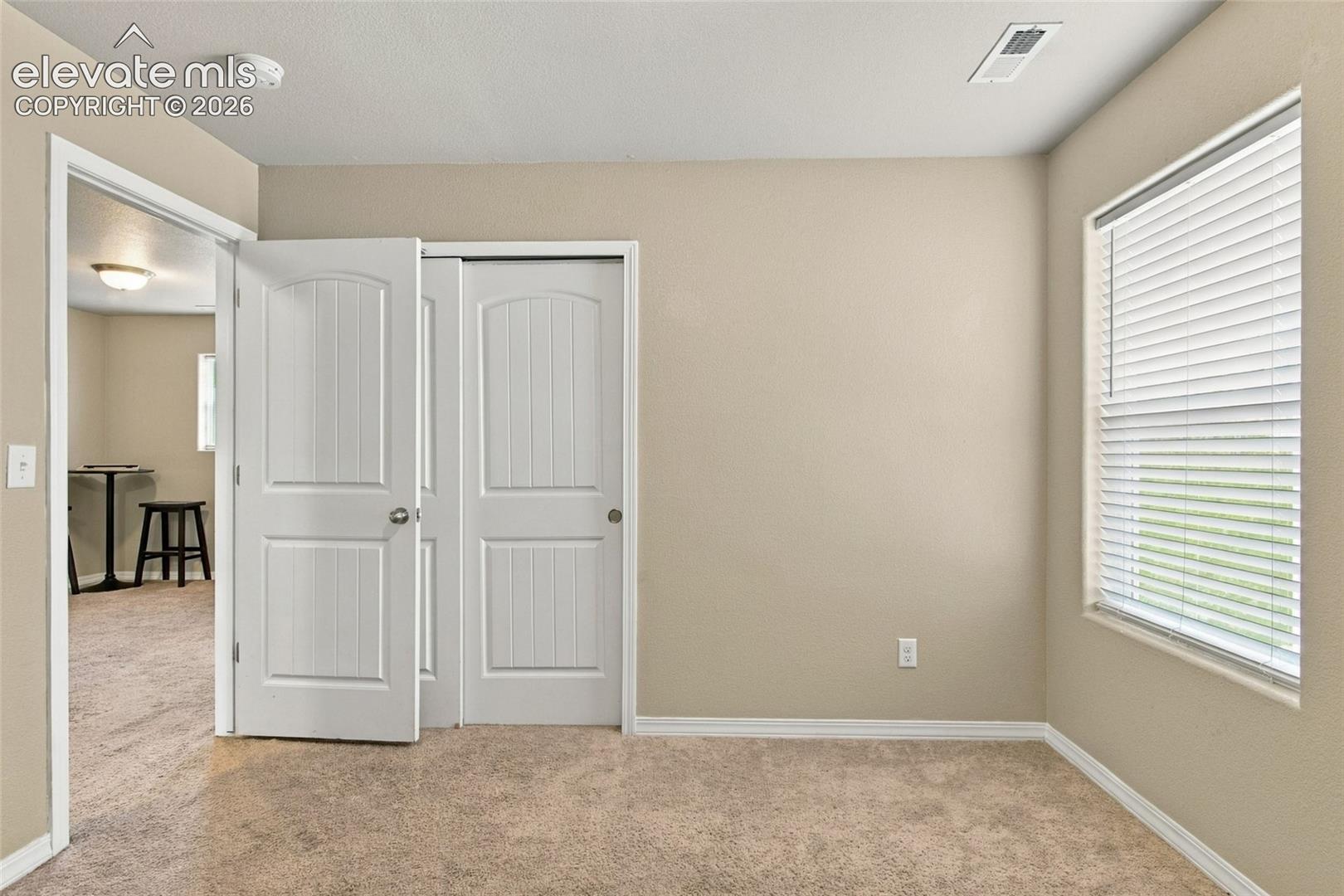 Neutral wall tones, carpeted flooring, two-panel arched interior doors, and a window with horizontal blinds