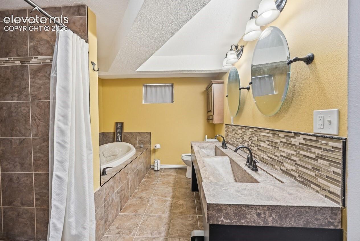 Dual vanity with integrated sinks, mosaic tile backsplash, jetted soaking tub, and a shower with tile surround