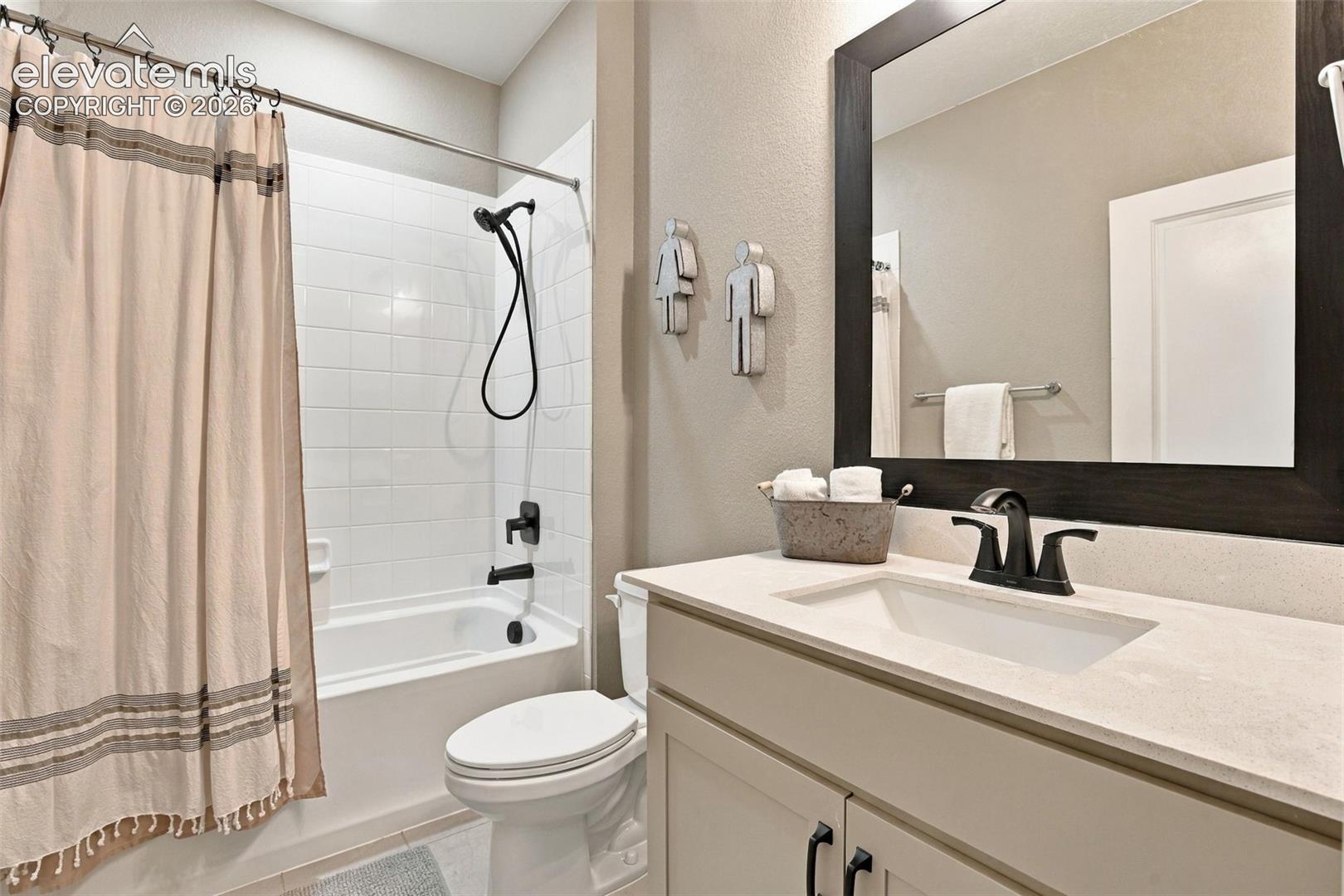 Bathroom featuring a vanity with a light-toned countertop, under-mount sink, and matte black hardware, accompanied by a soaking tub with white wall tile and a detachable showerhead