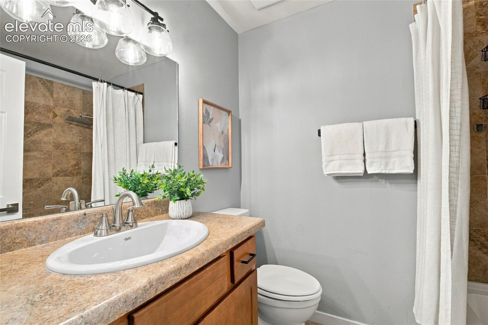 Bathroom featuring a vanity with a stone-finish countertop, undermount sink, multi-light fixture, and tile-surround shower