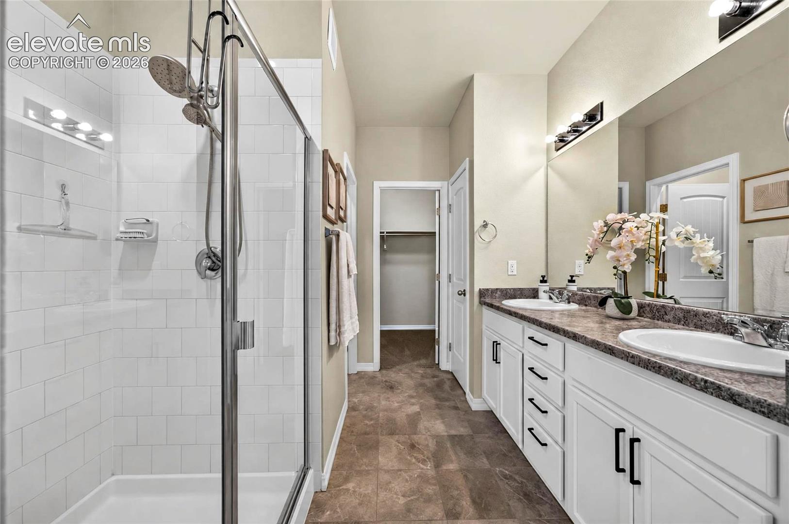 Dual vanity with integrated sinks, white cabinetry with dark hardware, and a walk-in shower with a glass enclosure