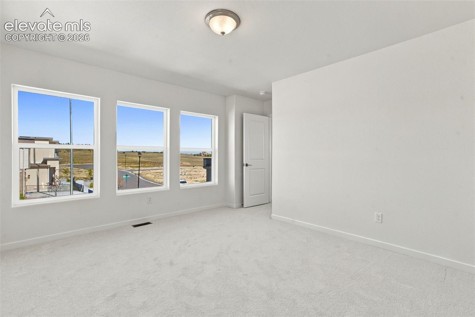 Light-colored carpeting, three large windows, and a flush mount ceiling light fixture
