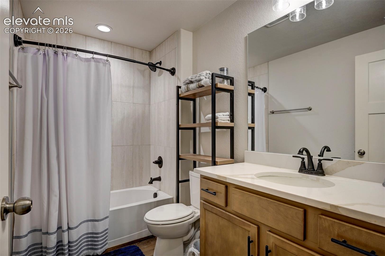 Bathroom featuring a tub/shower combination with tile surround, a wood-finish vanity with an integrated sink, a large vanity mirror, matte black fixtures, and a recessed ceiling light