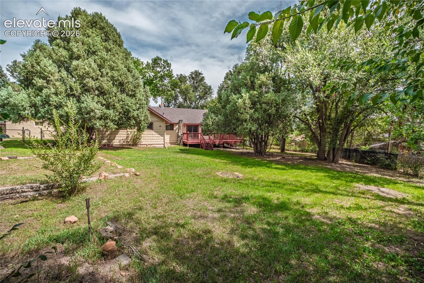 Expansive grassy yard with mature trees and a multi-level wood deck