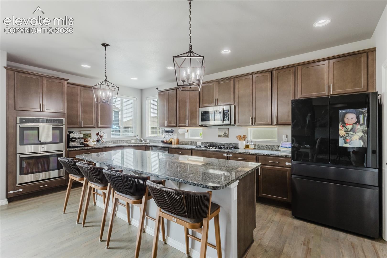 Spacious kitchen featuring a large island with a stone countertop, built-in double ovens, extensive wood cabinetry, and wood-finish flooring