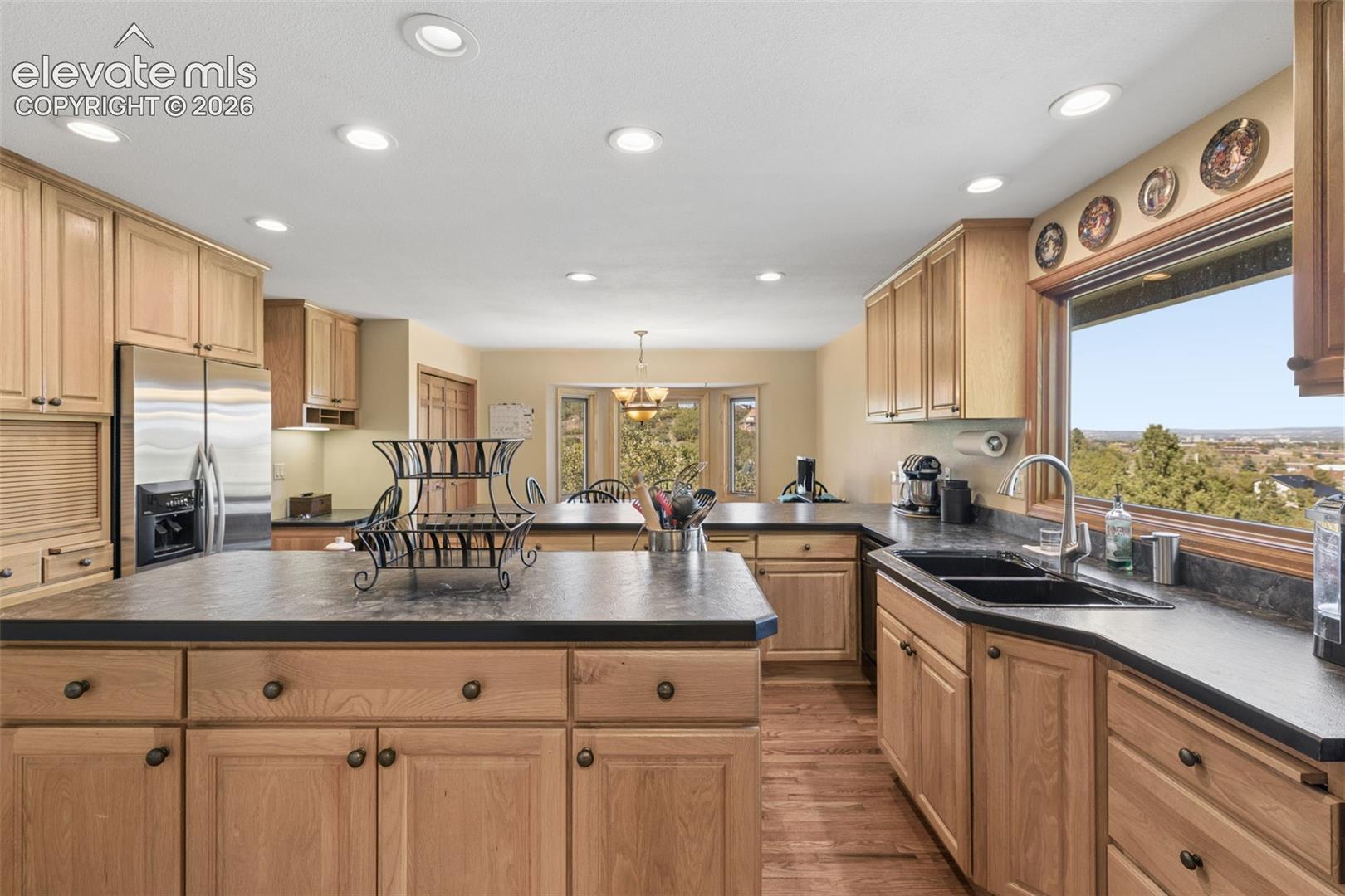 Kitchen featuring light-finish wood cabinetry, a central island, dark solid-surface countertops, stainless steel appliances, and recessed lighting