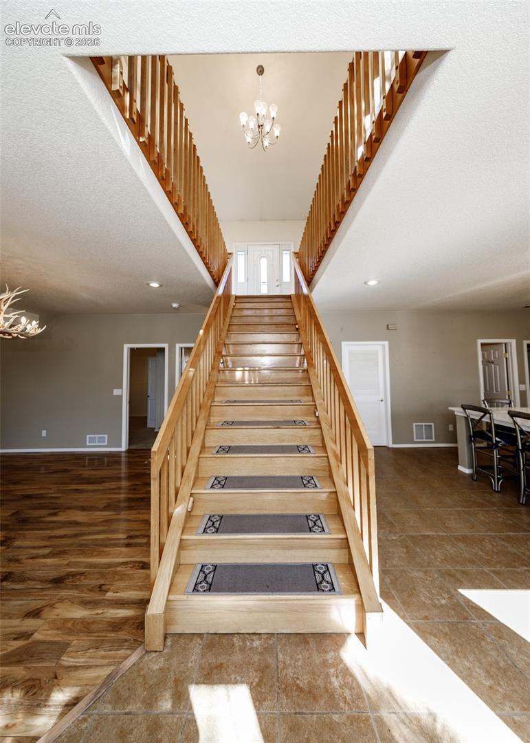 Grand foyer featuring a split staircase with wood railings, vaulted ceiling, and overhead chandelier