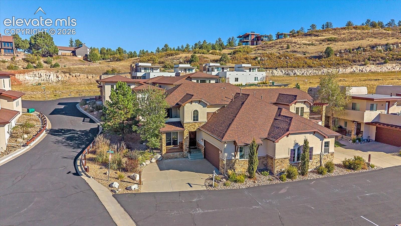 Multi-level residence featuring a stucco and stone exterior, steep-pitched roofline, attached multi-car garage, and xeriscaped lot