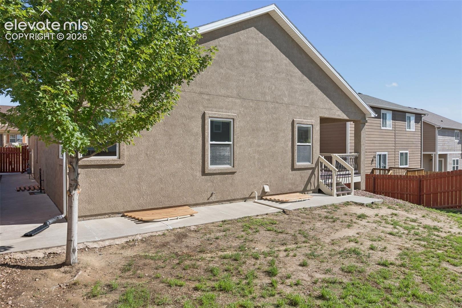 Brown stucco exterior featuring a covered porch with white railings and stairs, multiple windows, and a brown privacy fence
