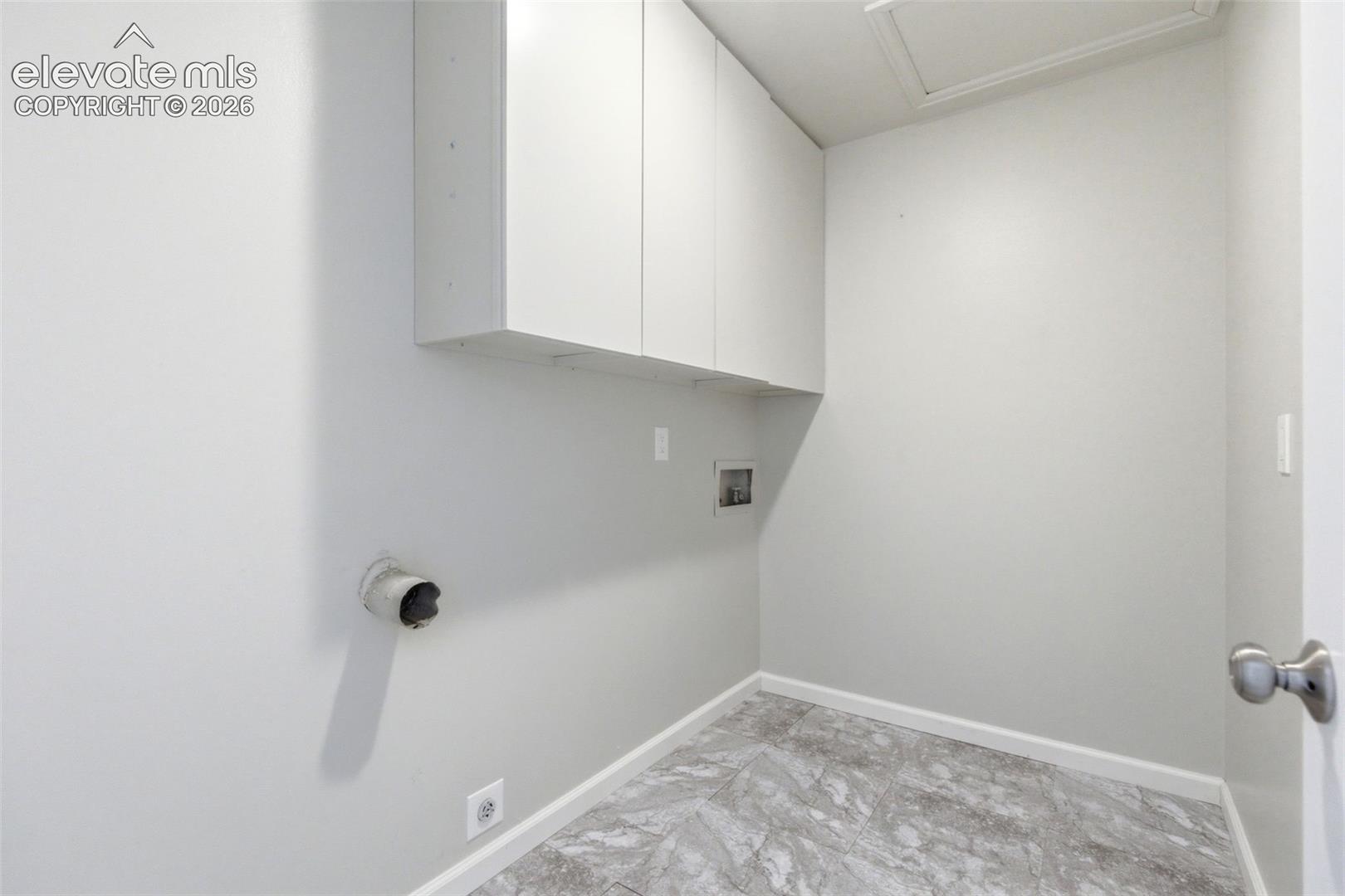 Utility space featuring overhead cabinetry, light gray walls, and gray stone-look flooring