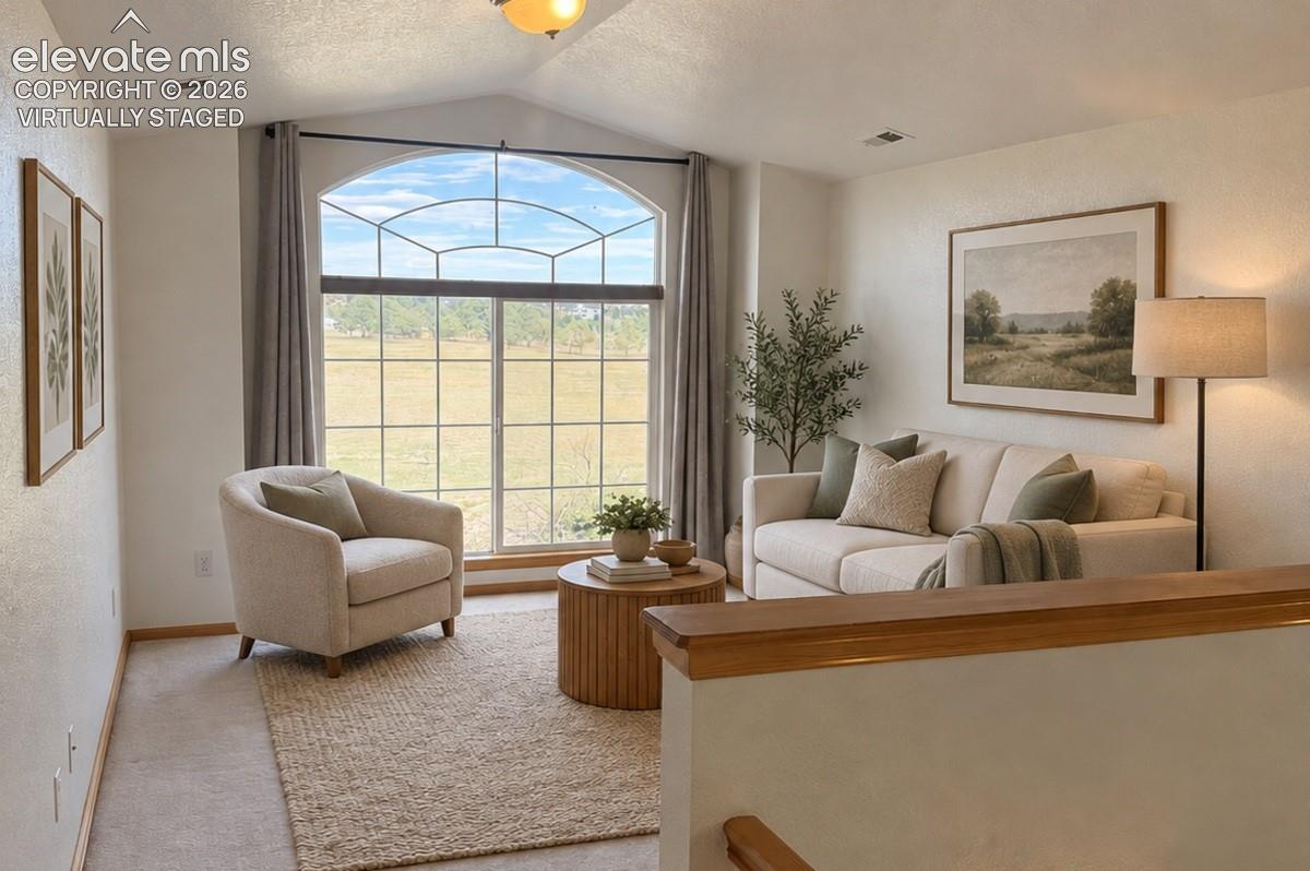 Vaulted ceiling, large arched window with grid pattern, light-toned wall paint, neutral carpeting, and wood-finish railing. Virtually staged.