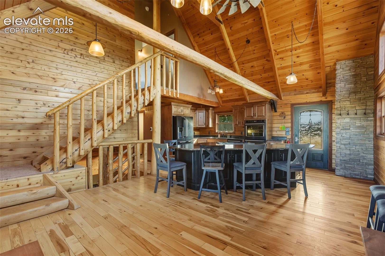 Vaulted wood-paneled ceiling, wood-finish flooring, stone accent wall, wood staircase with log railing, kitchen island with built-in seating