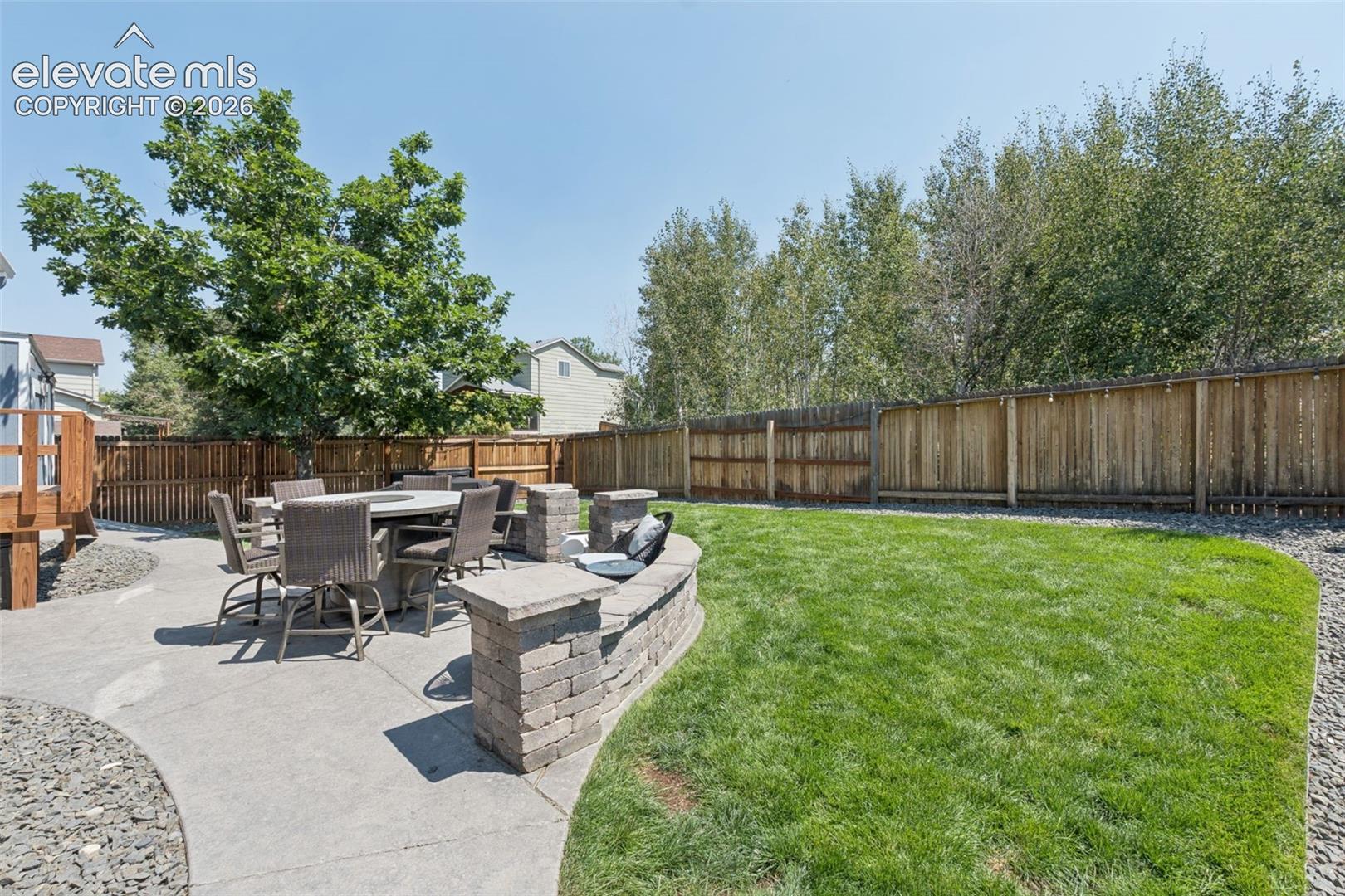 Expansive lawn area with a perimeter wood fence, large concrete patio, and a stone-clad retaining wall