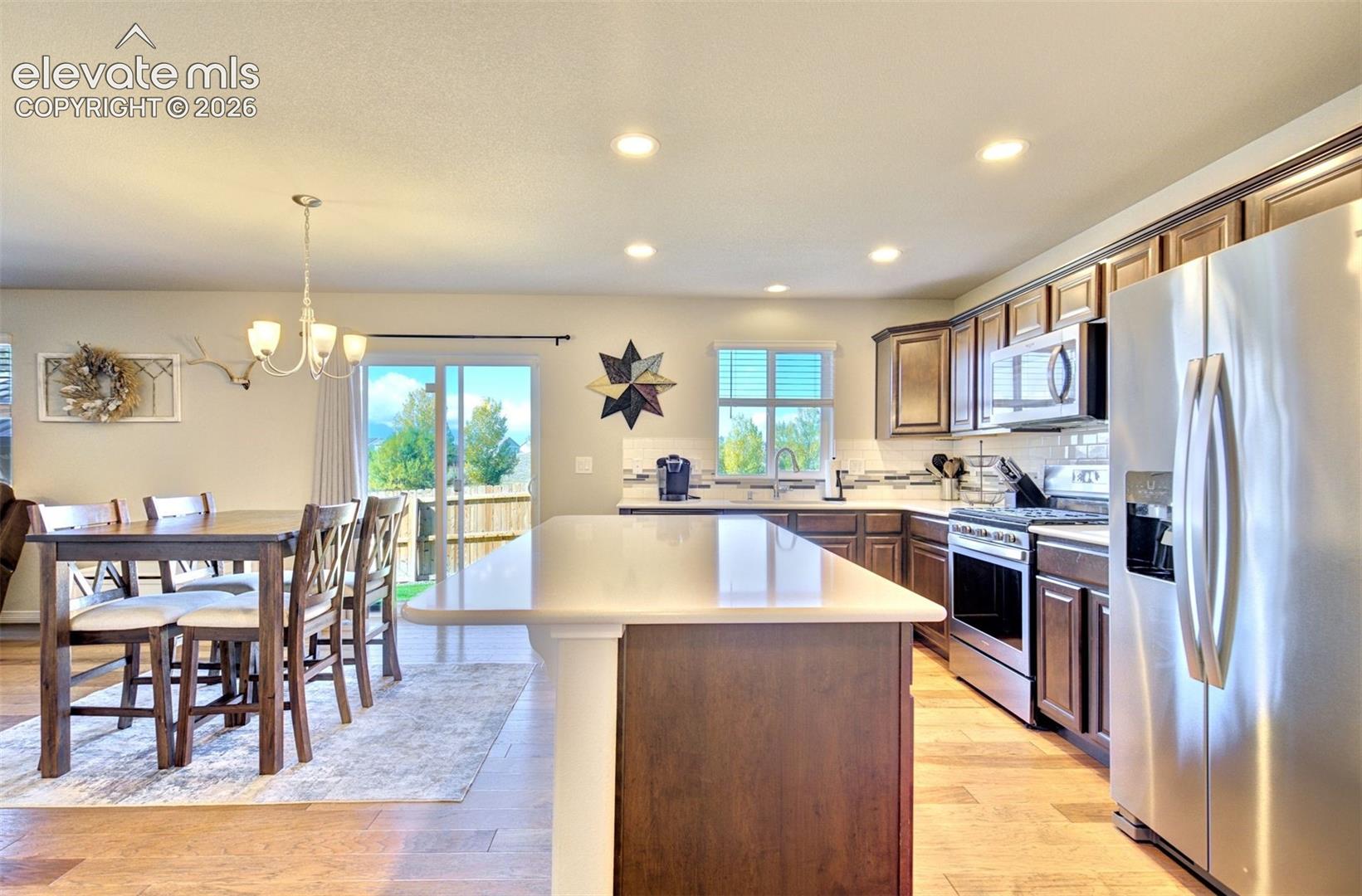 Kitchen featuring an island with a light-toned solid surface countertop, dark-finish cabinetry, stainless steel appliances, and wood-finish flooring
