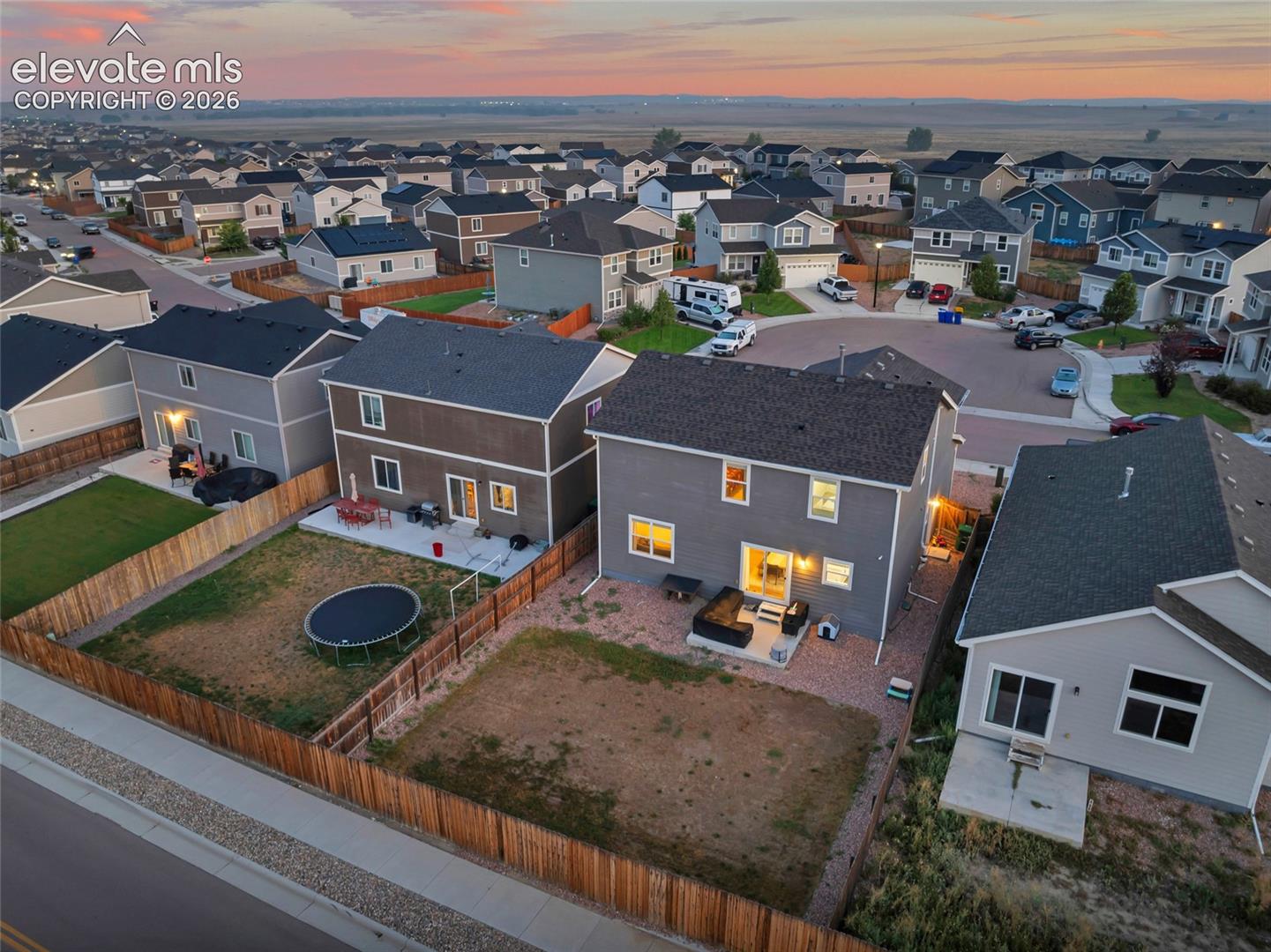 Modern residence featuring a contemporary brick and fiber cement exterior with illuminated window openings, pitched roofline with architectural shingles, and a fenced yard with mature landscaping