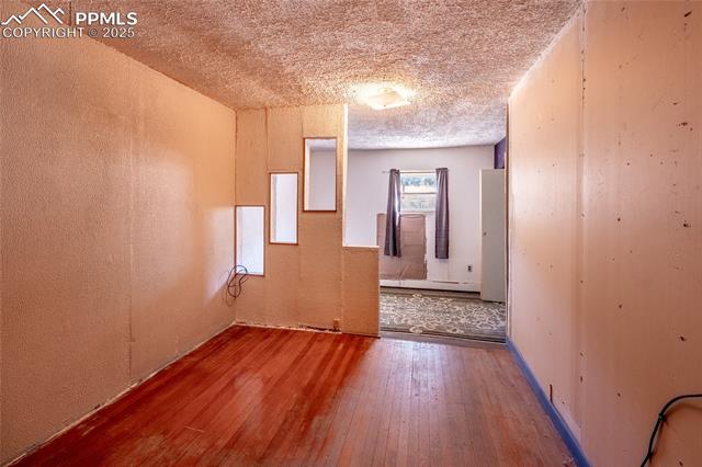 Empty room featuring a textured ceiling, hardwood / wood-style floors, a textured wall, and a baseboard heating unit