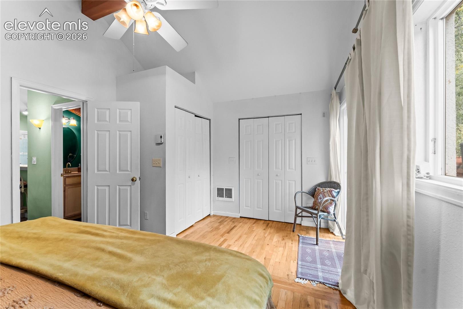 Vaulted ceiling with a central paddle fan, wood-finish flooring, and dual bi-fold closet doors