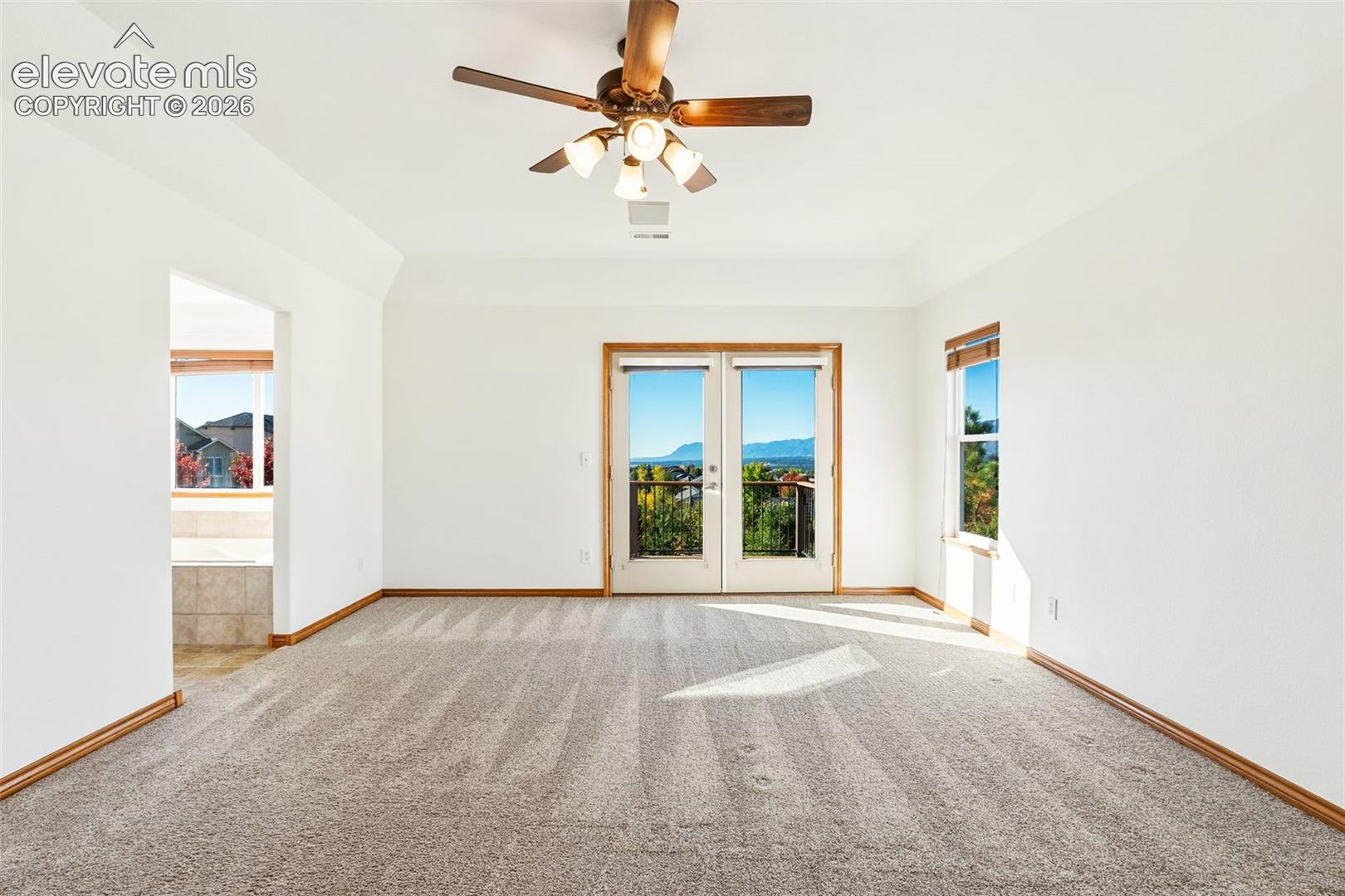 Tray ceiling, neutral carpeting, ceiling fan with integrated lighting, and glass-paneled doors providing exterior access