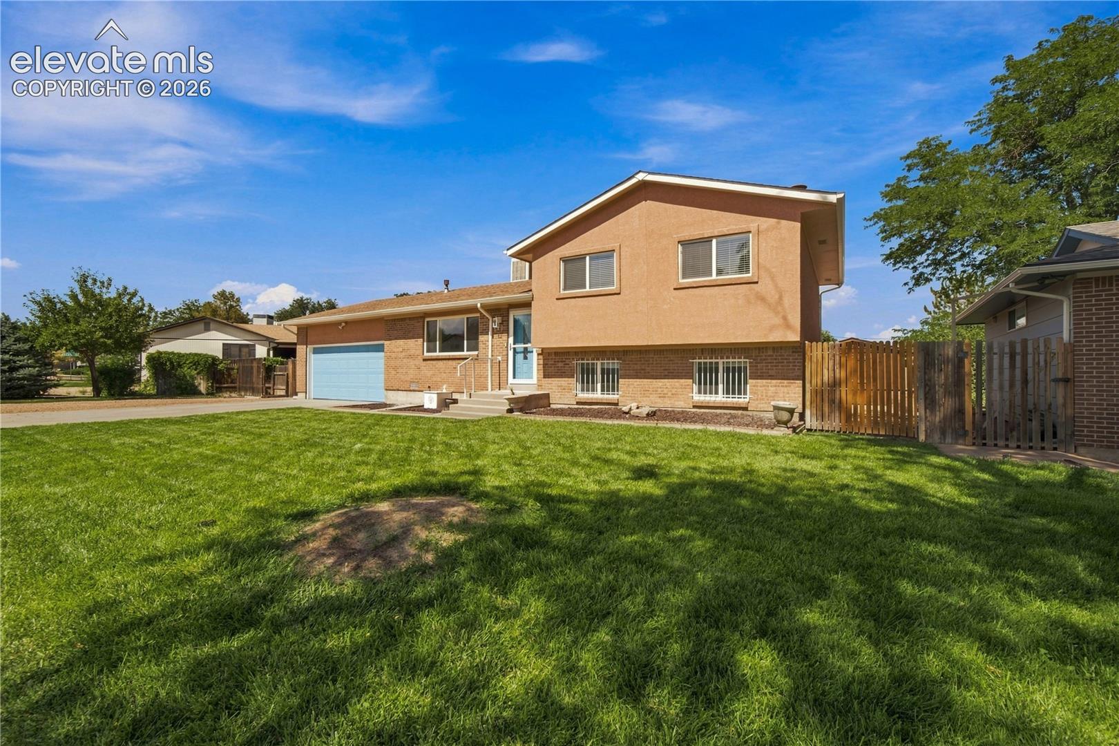 Two-story stucco and brick exterior featuring a front-facing garage, a concrete driveway, and a wooden fence
