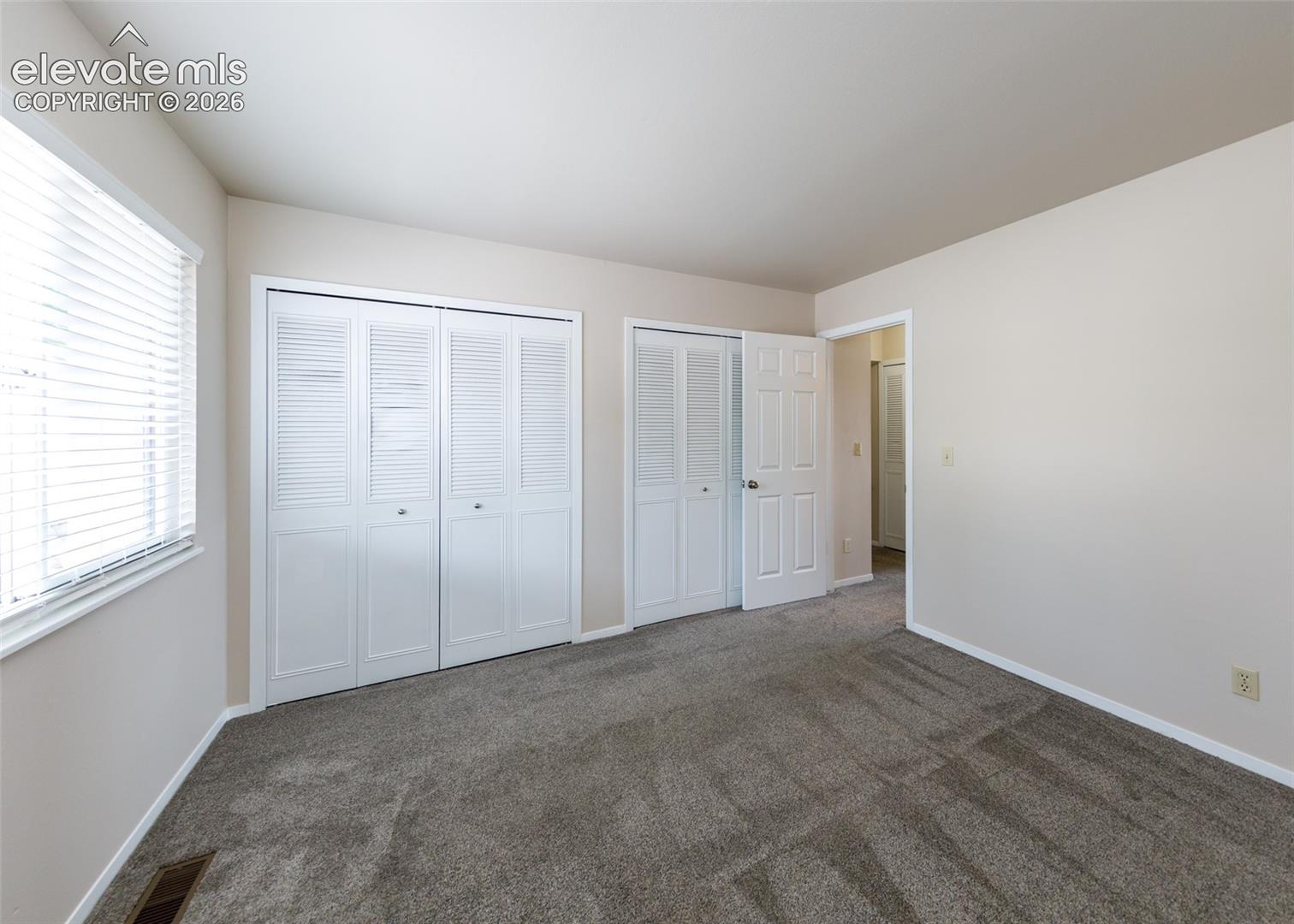 Neutral wall paint, window with blinds, carpeted flooring, and white bi-fold closet doors