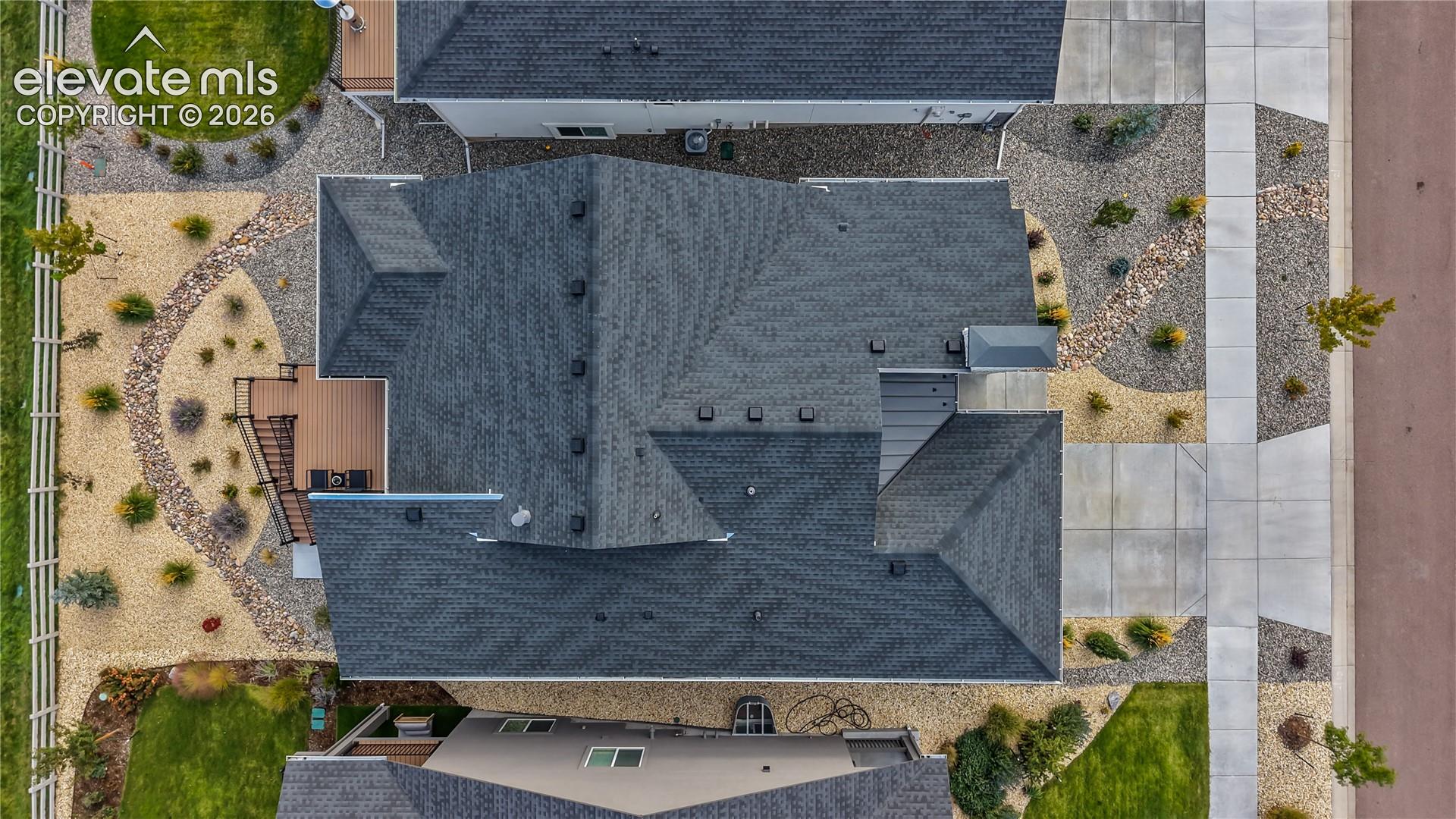 Aerial view of property featuring a multi-gabled shingle roof, paved concrete driveway, xeriscaped lot, elevated wood-finish deck, and wood fence