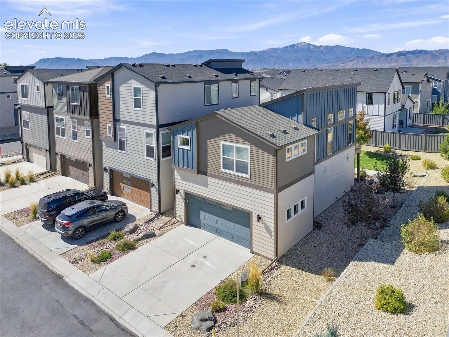 Multi-story exterior featuring composite siding, attached two-car garages, concrete driveways, and mountain backdrop