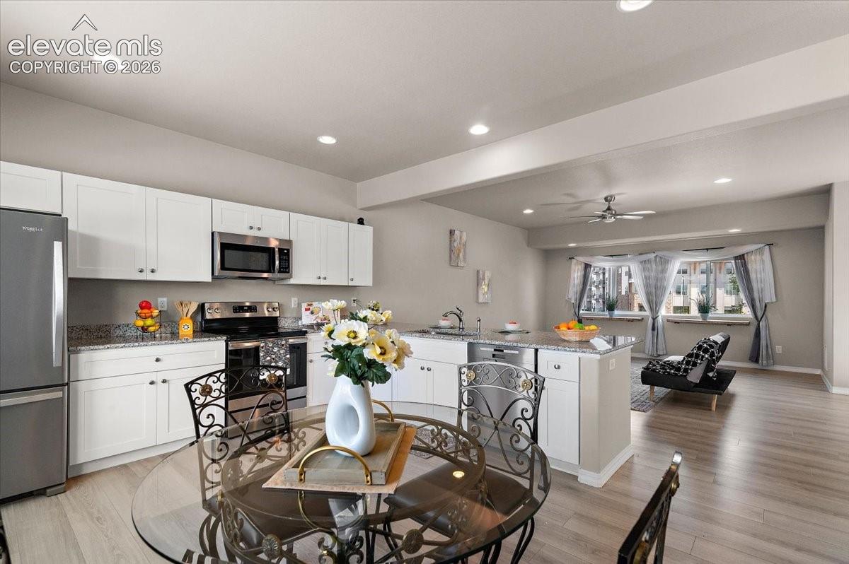 Open-concept kitchen featuring white cabinetry, stainless steel appliances, and granite countertops