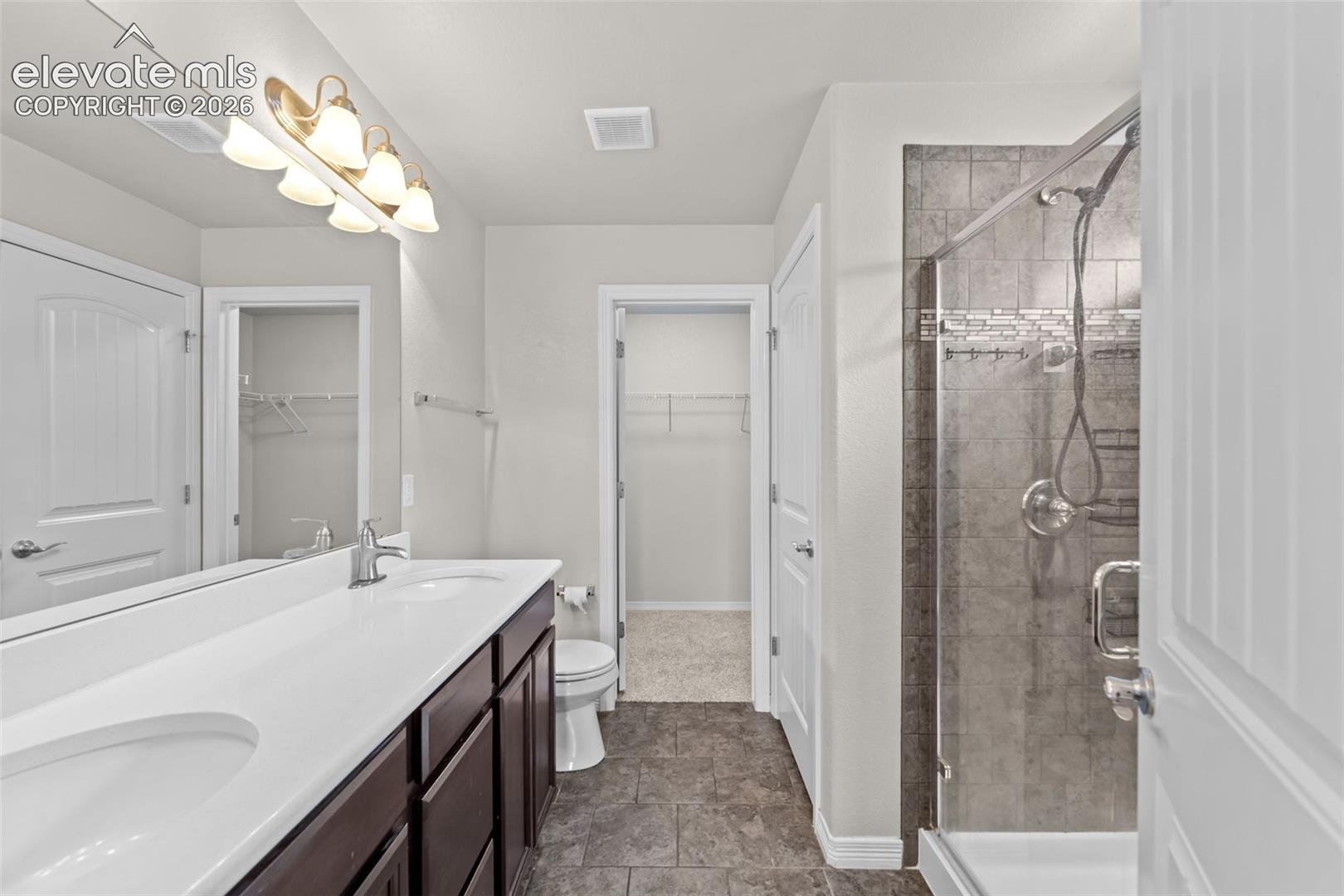 Dual sink vanity with dark wood-finish cabinetry, a framed shower with tile surround, and tile flooring