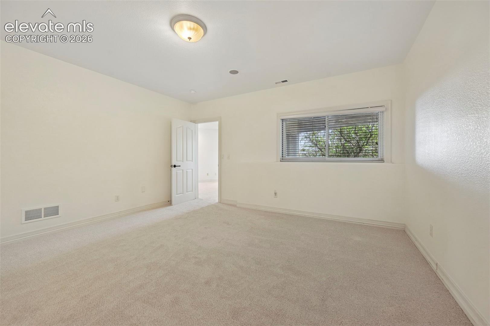 Carpeted room featuring a window with horizontal blinds, a white paneled door with black hardware, and a ceiling-mounted light fixture