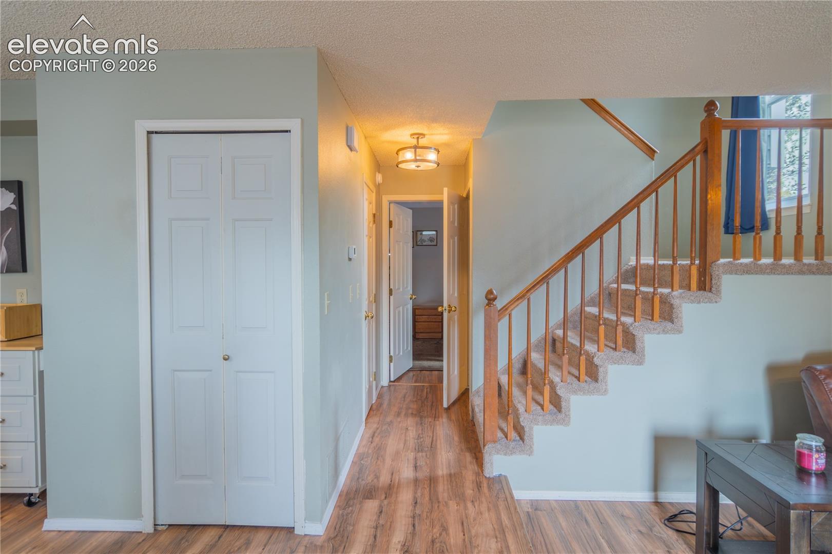 Wood-finish flooring throughout, carpeted staircase with wood banister and balusters, and a paneled bifold door