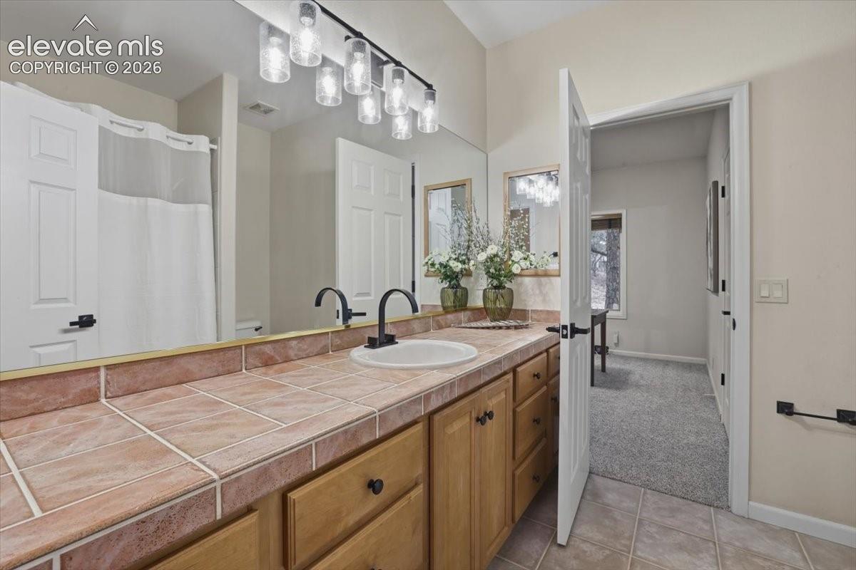 Tile countertop with integrated sink, wood-finish cabinetry, dual matte black faucets, and a full-width mirror