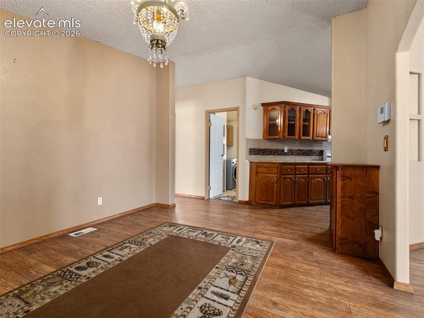 Wood-finish flooring, decorative crystal chandelier, and natural wood cabinetry with stone-surface countertops