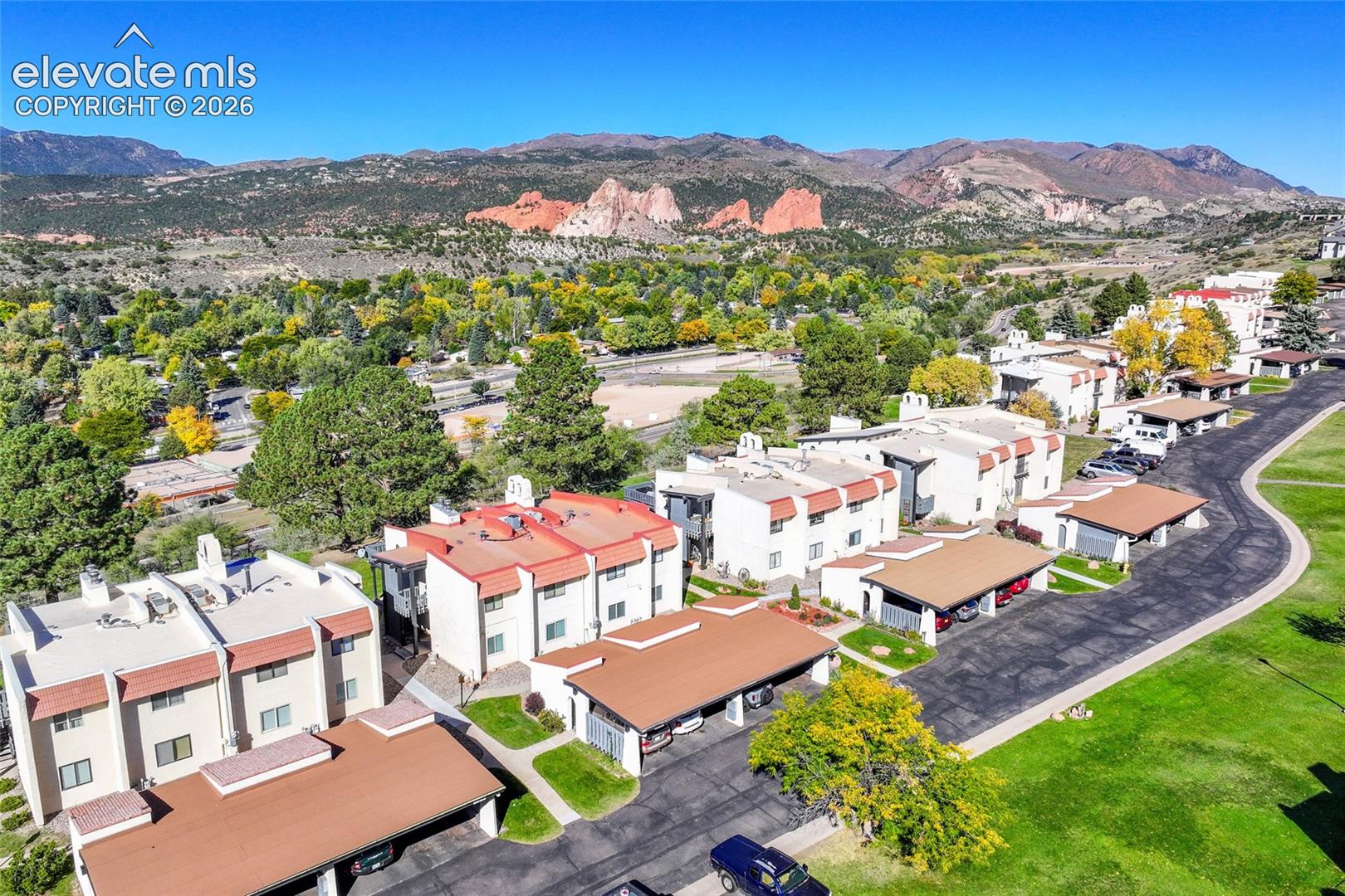 Multi-story residential structures featuring exterior stucco facades, pitched roofing, and attached covered parking areas, set against a backdrop of mountainous terrain