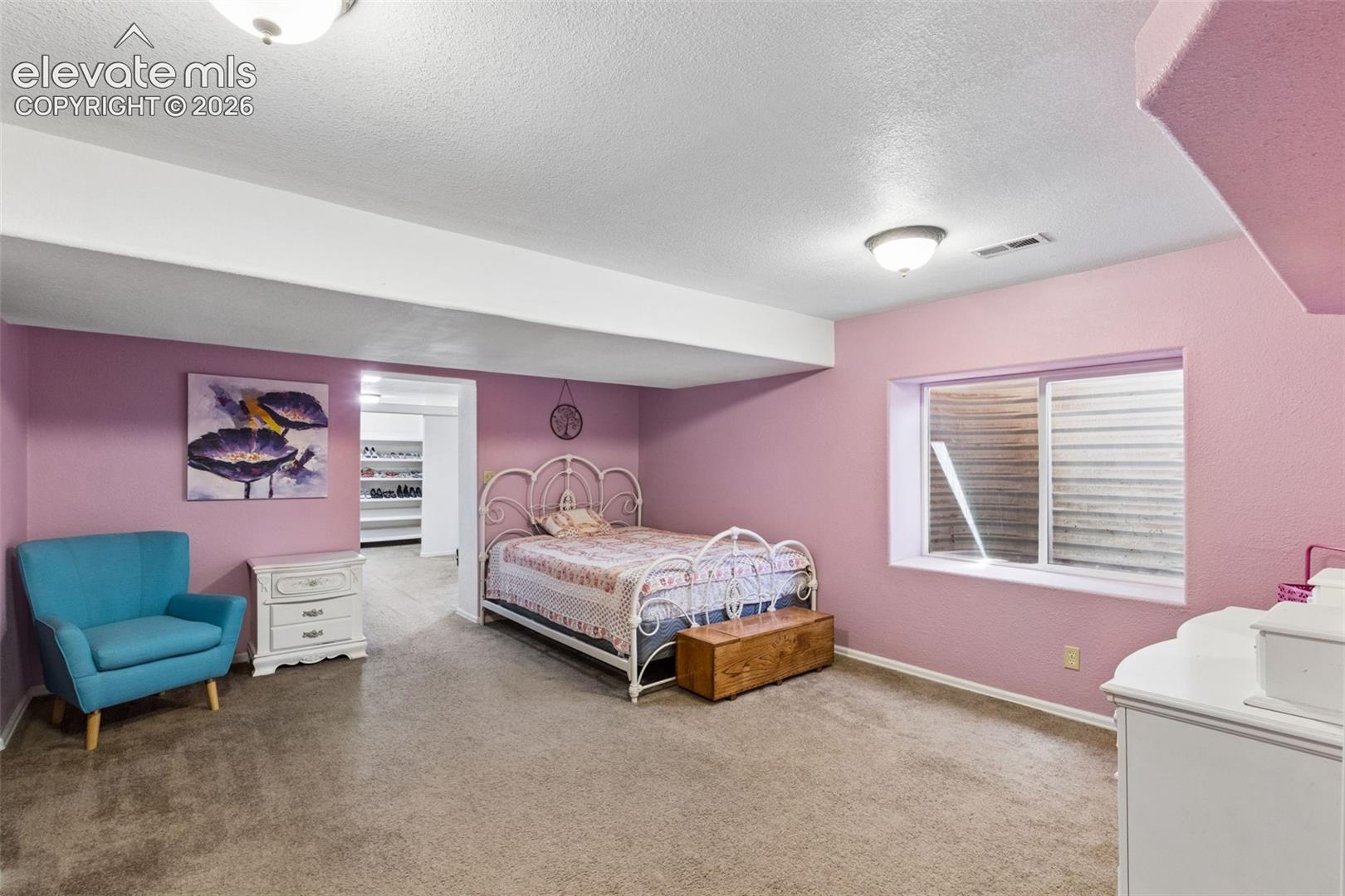 Bedroom interior featuring neutral wall-to-wall carpeting, dual flush-mount ceiling light fixtures, and a recessed window with an egress well