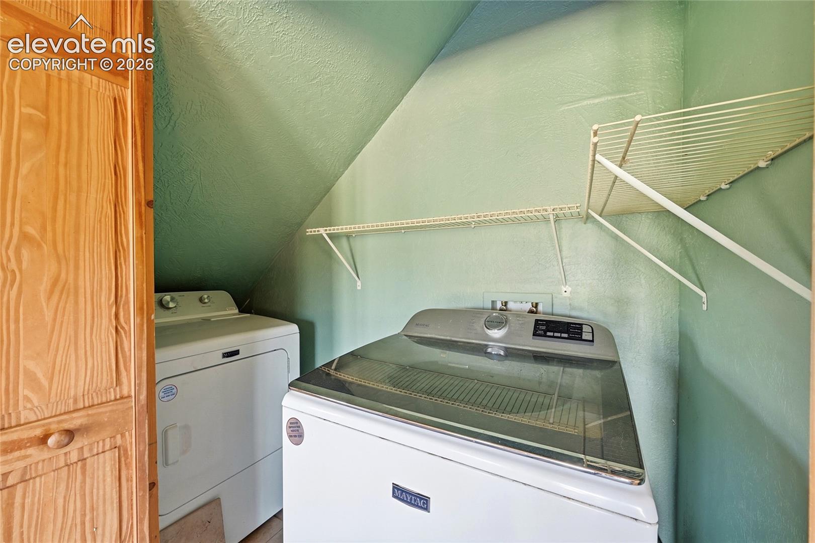 Dedicated laundry space featuring a sloped ceiling, two wall-mounted storage shelves, and wood-finish cabinetry