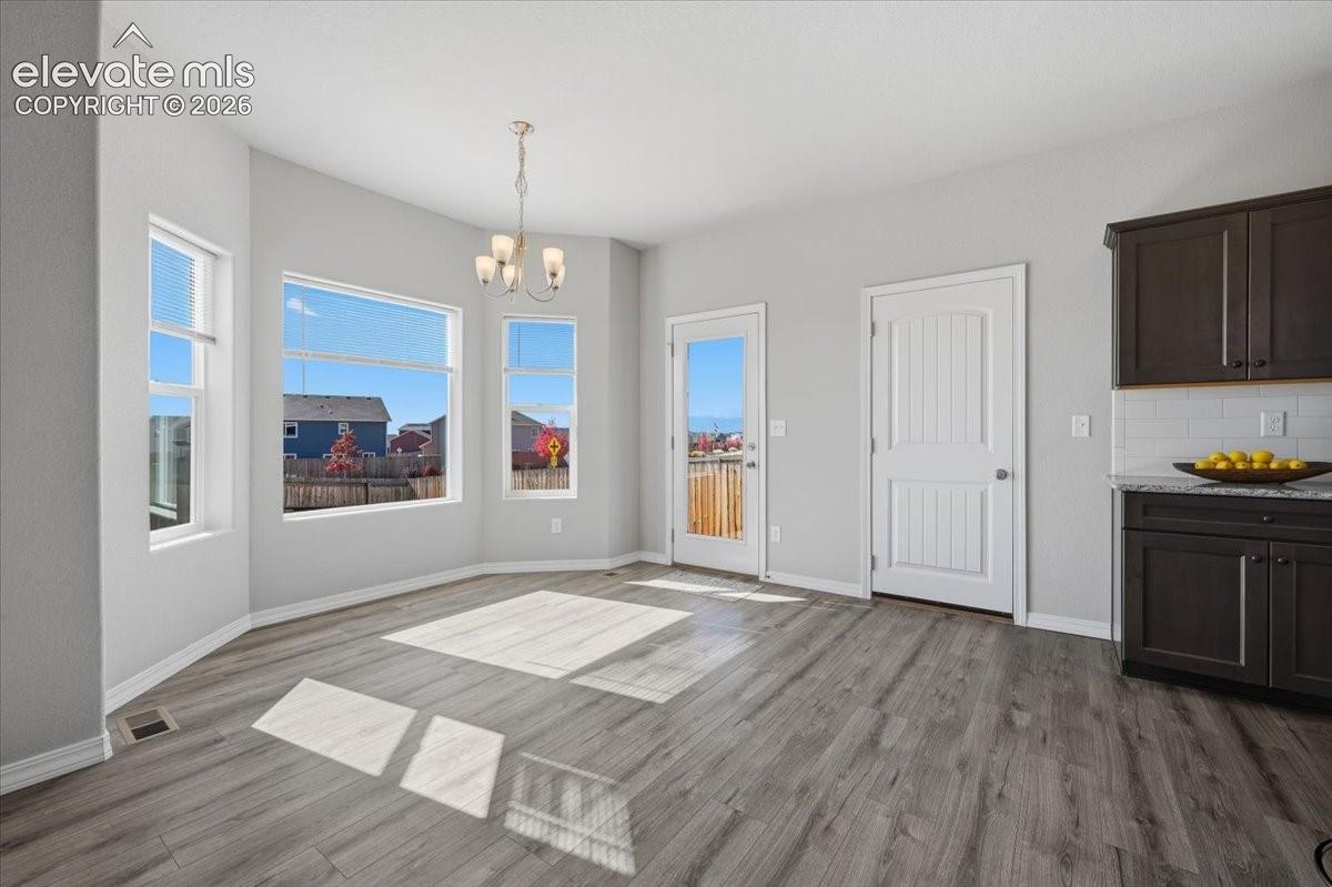 Dining area featuring wood-finish flooring, a multi-paneled bay window, dark cabinetry with stone-finish countertops, and an integrated glass-panel door