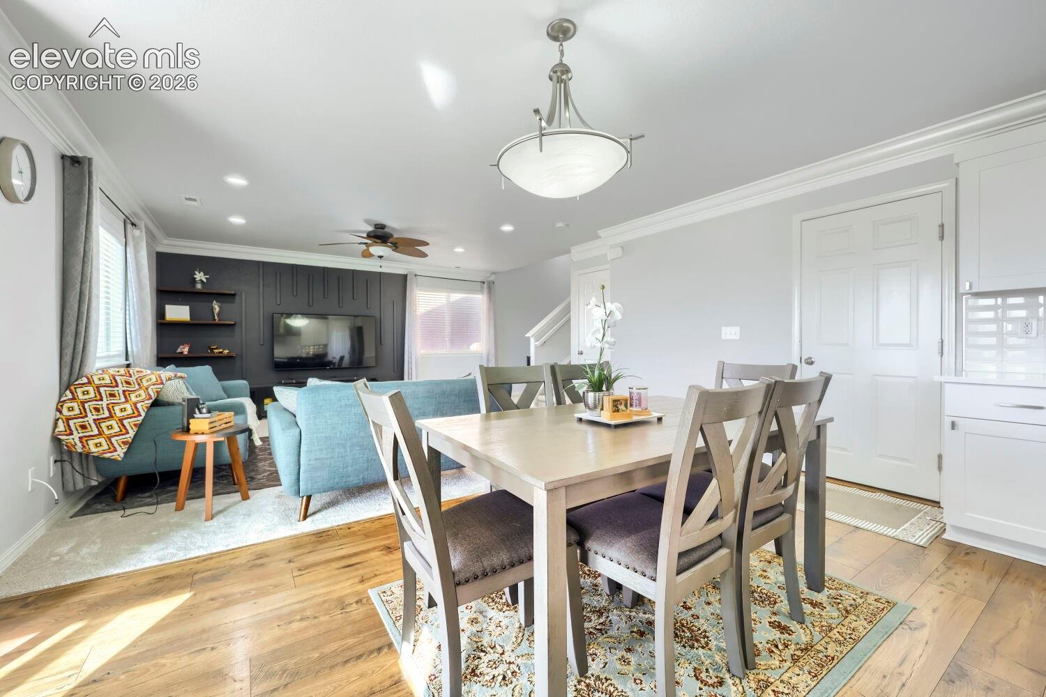 Open-concept area featuring wood-finish flooring, crown molding, recessed lighting, a decorative wall panel accent, and a polished nickel chandelier