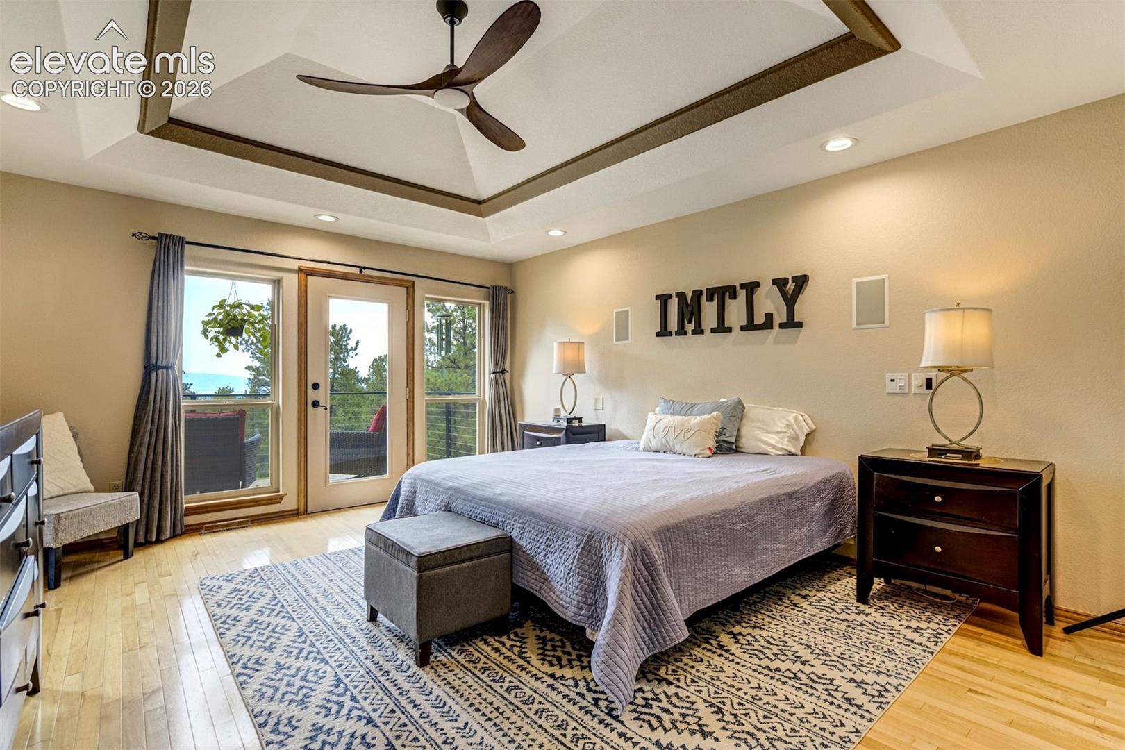 Tray ceiling with recessed lighting and a ceiling fan, hardwood flooring, and a glass-paneled door leading to an exterior balcony