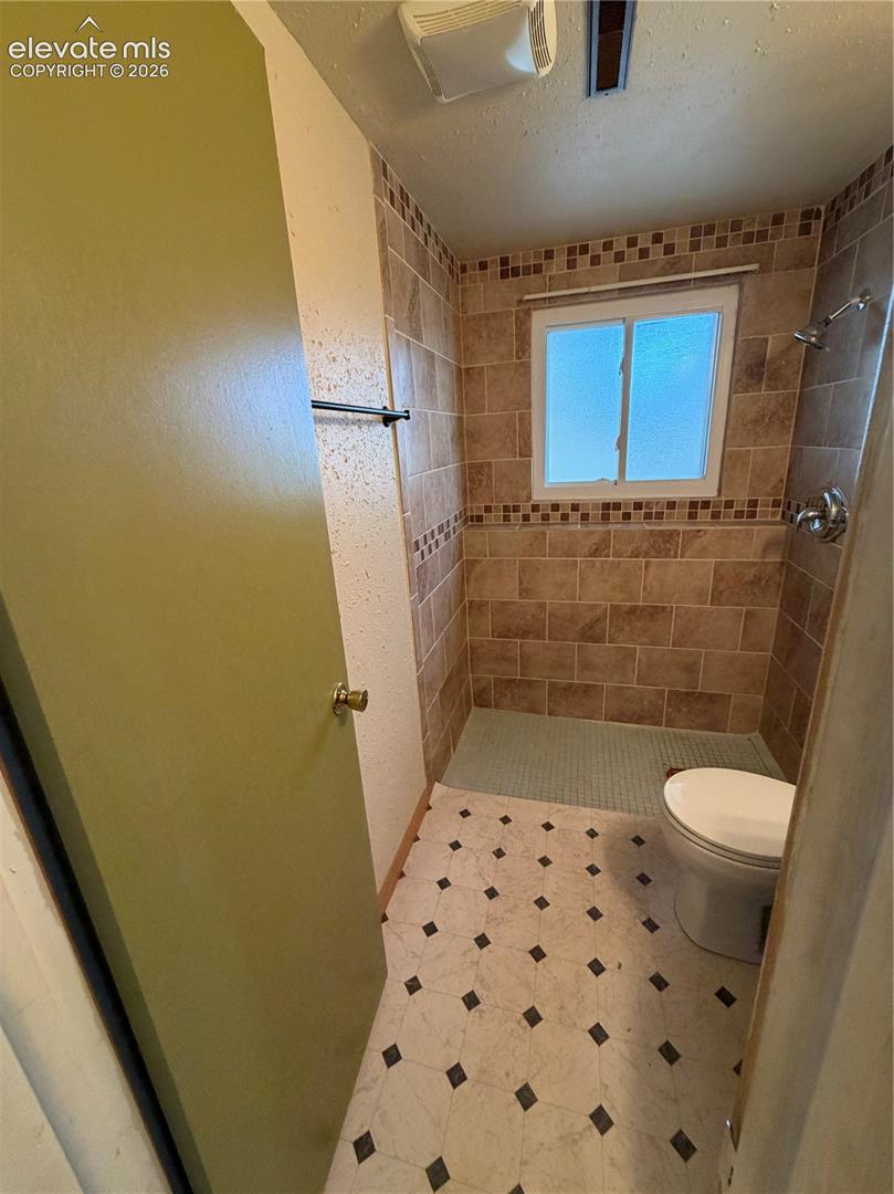 Full-height tiled shower surround with decorative accent border, integrated shower head, window with natural light, and tile flooring with diamond inlay pattern