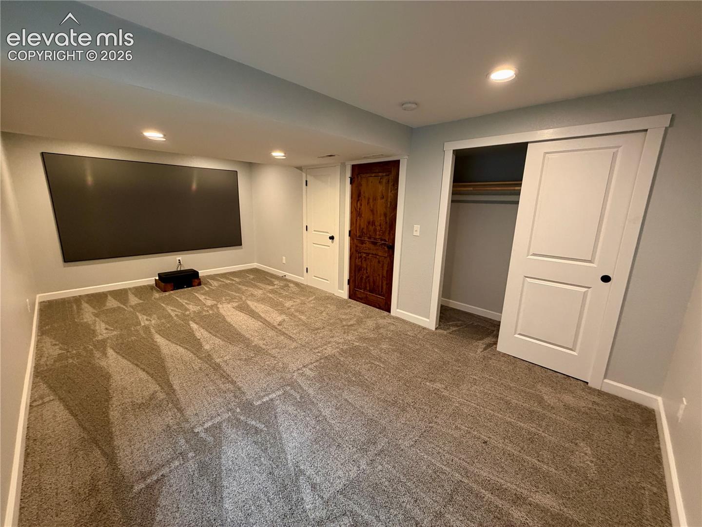 Picture with furniture removed. Wall-mounted projection screen above neutral-toned carpeting