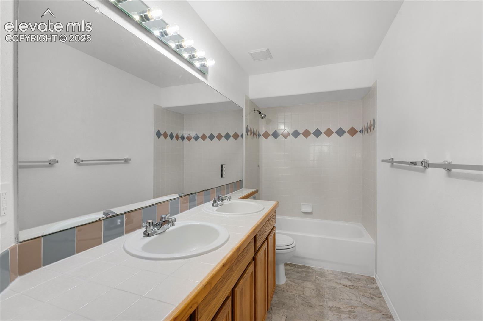 Dual vanity with integrated sinks, wood-finish cabinetry, full-width mirror, and overhead lighting