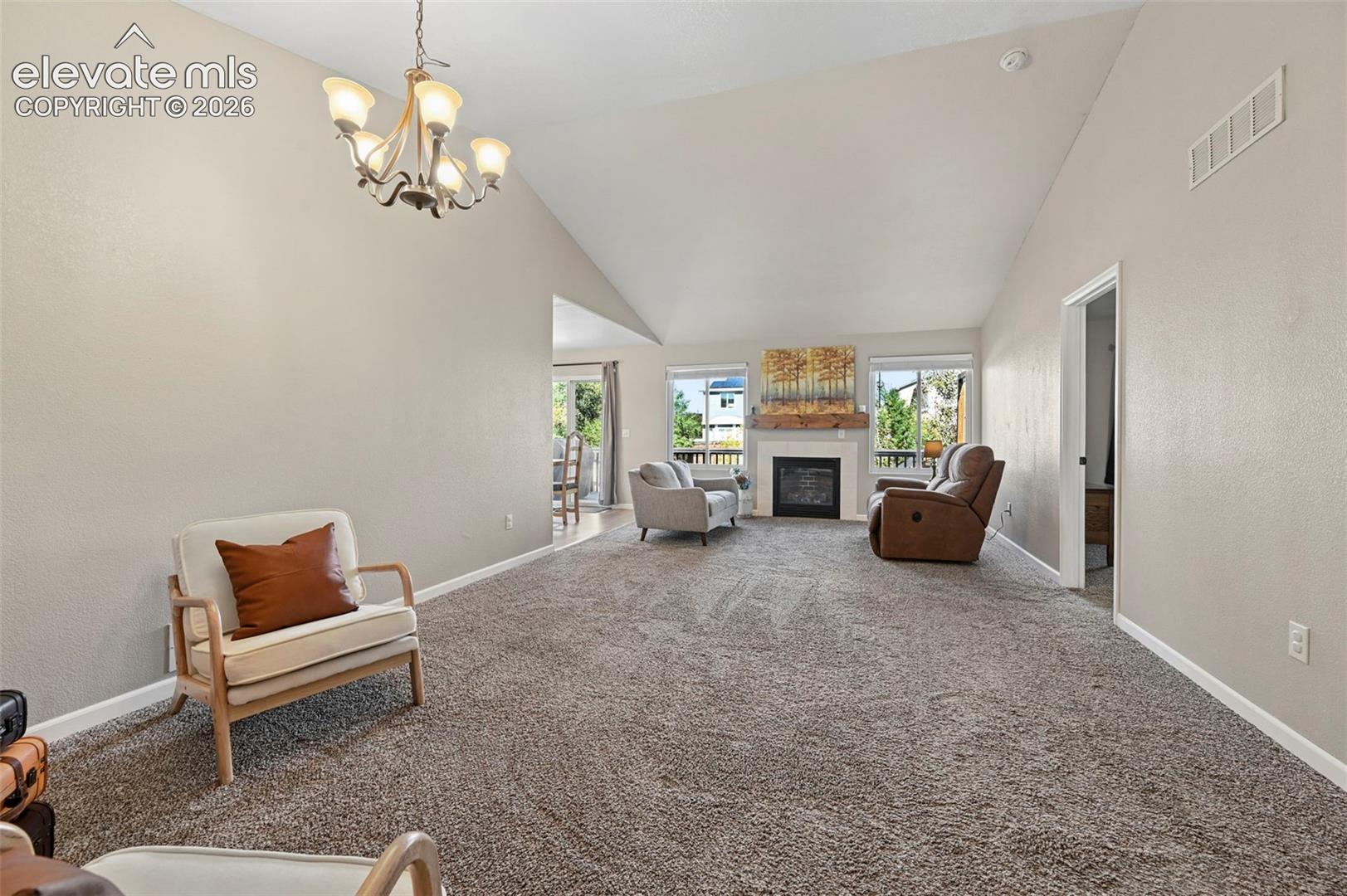Vaulted ceilings, fireplace with a wood mantel, multi-arm chandelier, and neutral wall tones