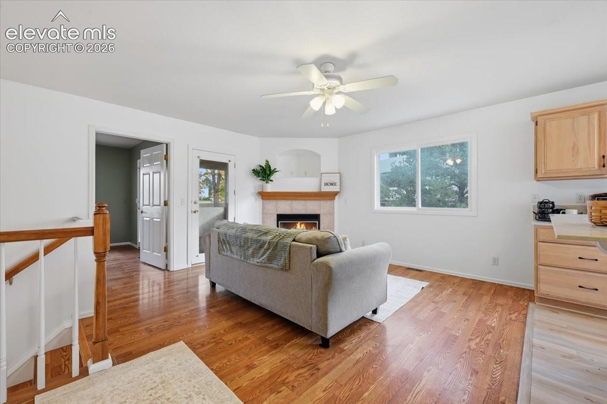 Wood-finish flooring, fireplace with a tile surround and wooden mantel, ceiling fan with light fixture, and wooden cabinetry