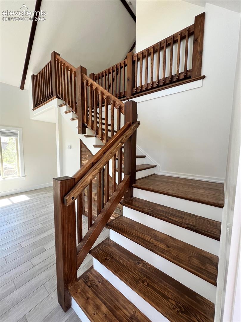 Staircase featuring rich wood-finish treads and balusters, white risers, and a vaulted ceiling with exposed beams