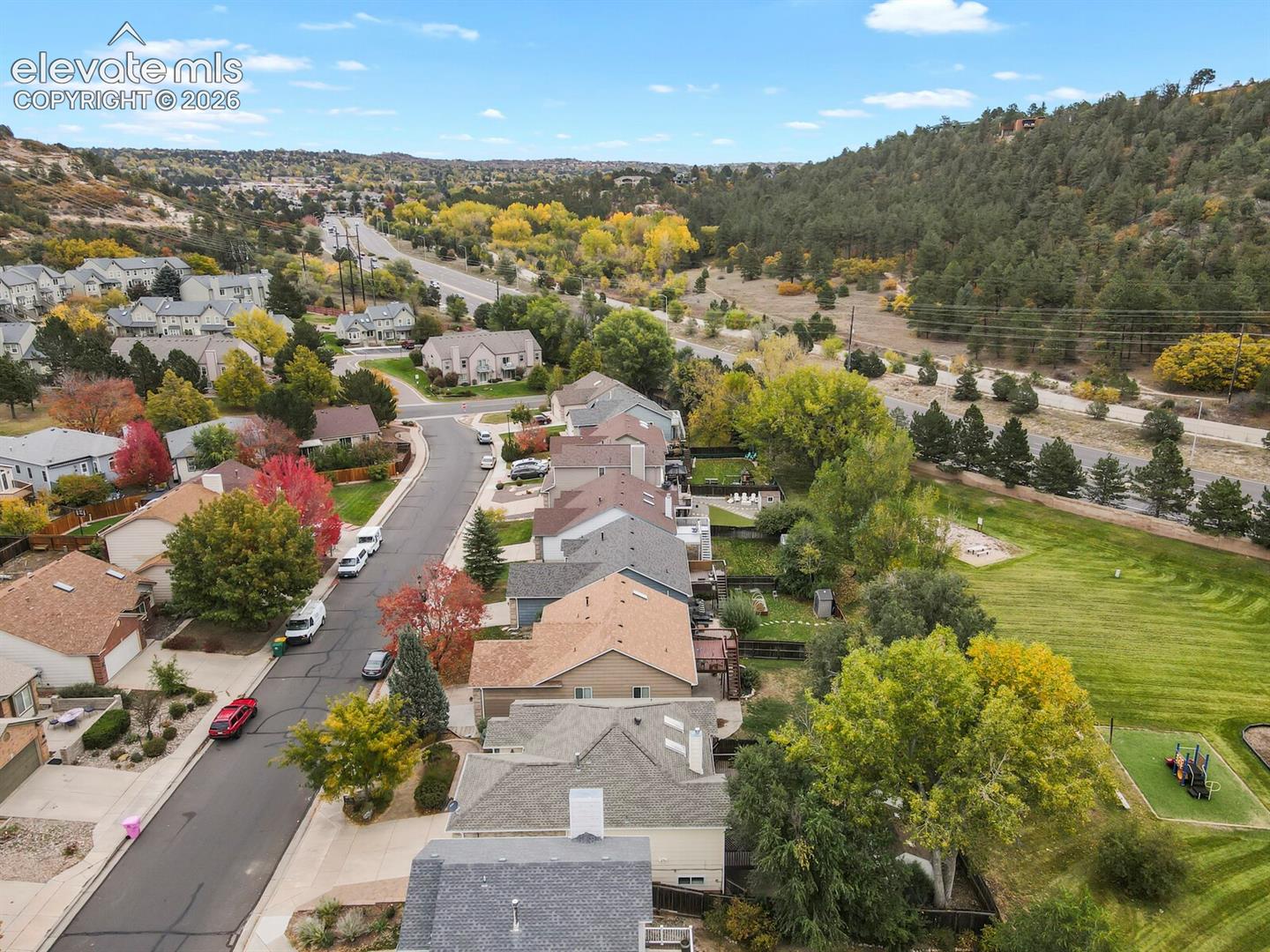 Aerial perspective of suburban residential neighborhood featuring asphalt paved streets, mature deciduous and evergreen trees, and sloped hillside terrain