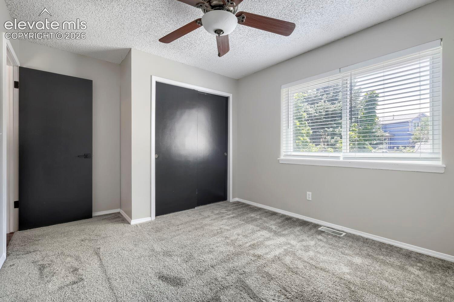Carpeted room featuring a ceiling fan, two windows with blinds, a solid black interior door, and a black sliding closet door